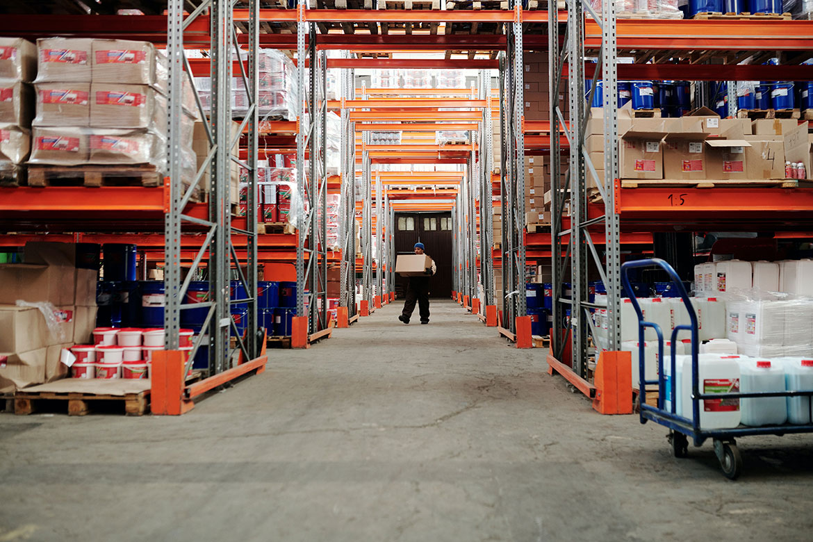 Image of man holding box in aisle of distribution center