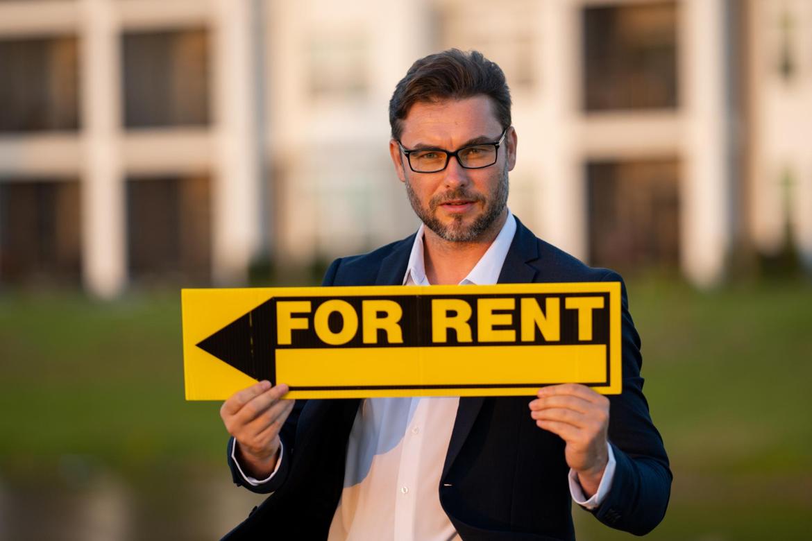 A man in a suit holding a For Rent sign
