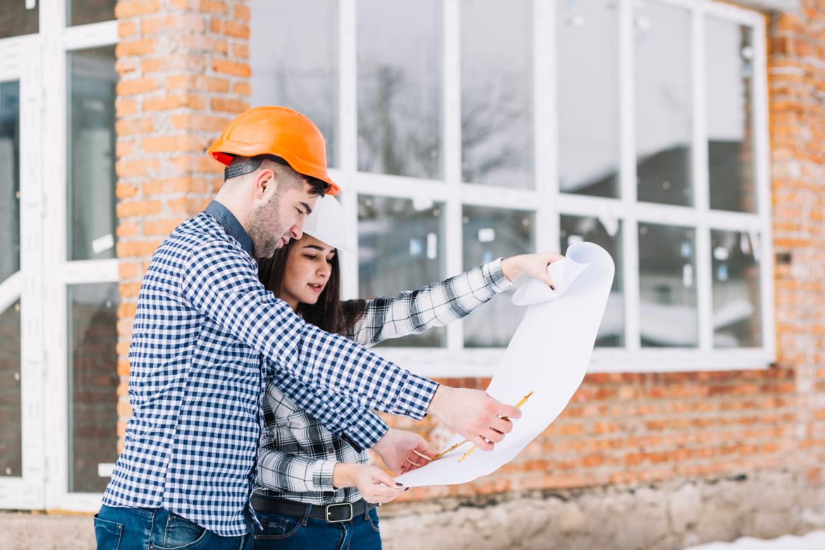 Couple looking at a plan in front of a house under construction.